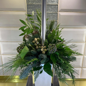 Christmas centrepiece in a festive vase with mixed foliage and a candle