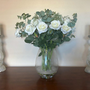 Large vase arrangement of white roses and eucalyptus in a vase with 2 white candlesticks framing it