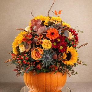 Floral pumpkin arrangement using seasonal flowers and foliage. Roses, Gerbera, Sunflowers, Thistle, Hypericum, Crysanthemum. Eucalyptus, and Ivy