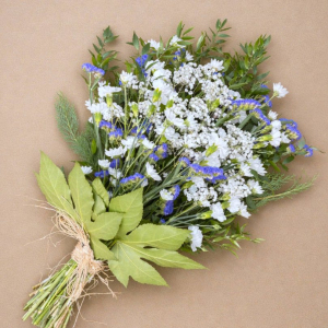 A hand tied flat bouquet including, statice, carnations, chrysanthemum, gypsophilia and soft ruscus and fatsia leaves, finished with a raffia bow