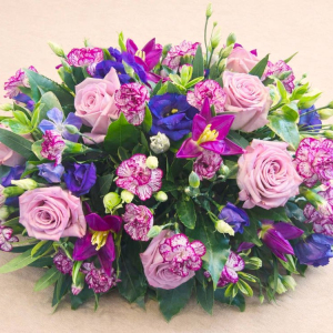 Casket spray with lilac roses, mauve tulips, purple lisianthus and mauve carnations with mixed foliage