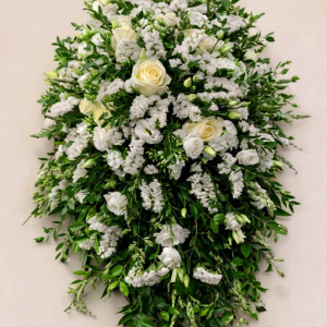 casket spray with green foliage cradling white and yellow flowers