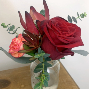 small posy with red rose, green foliage, standing in glass